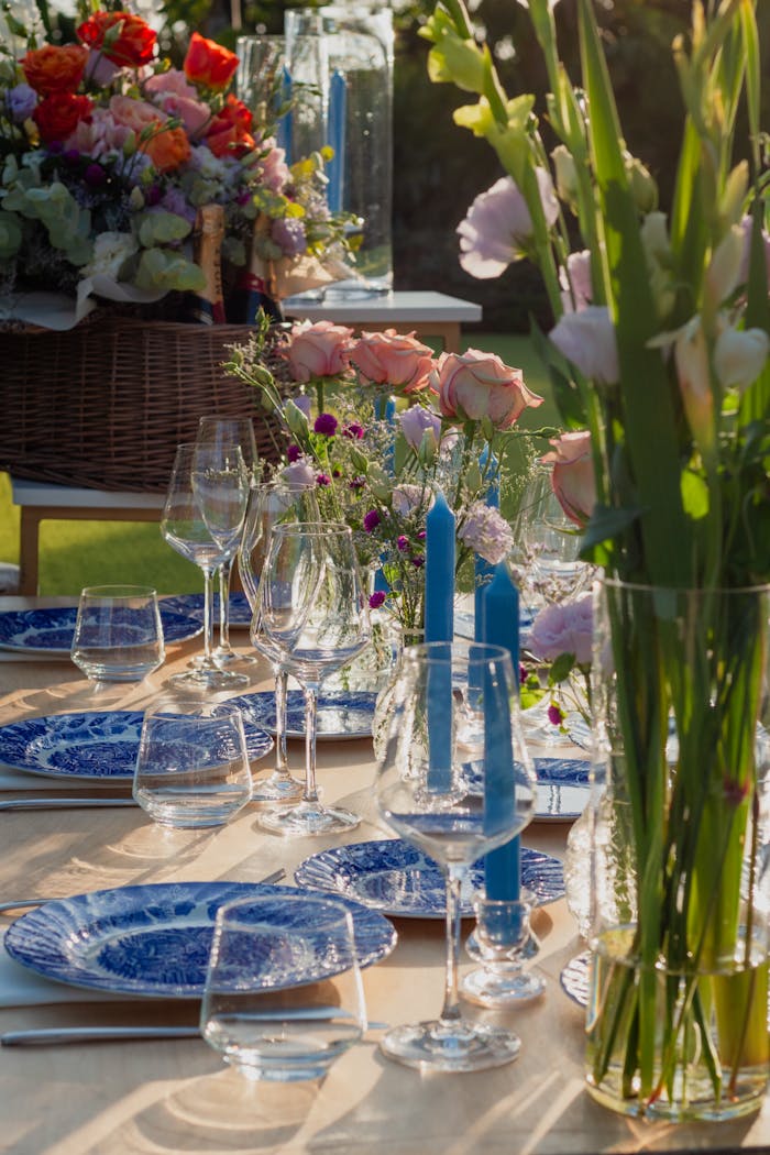 Elegant outdoor dining setup with blue plates, glassware, and vibrant floral centerpiece.